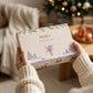 Coffret Rituels de Noël tenu entre les mains, devant le sapin